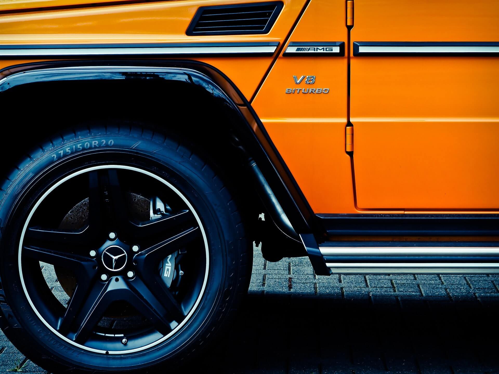 Striking black front left wheel, brilliant partial door and shiny silver running board of an orange SUV