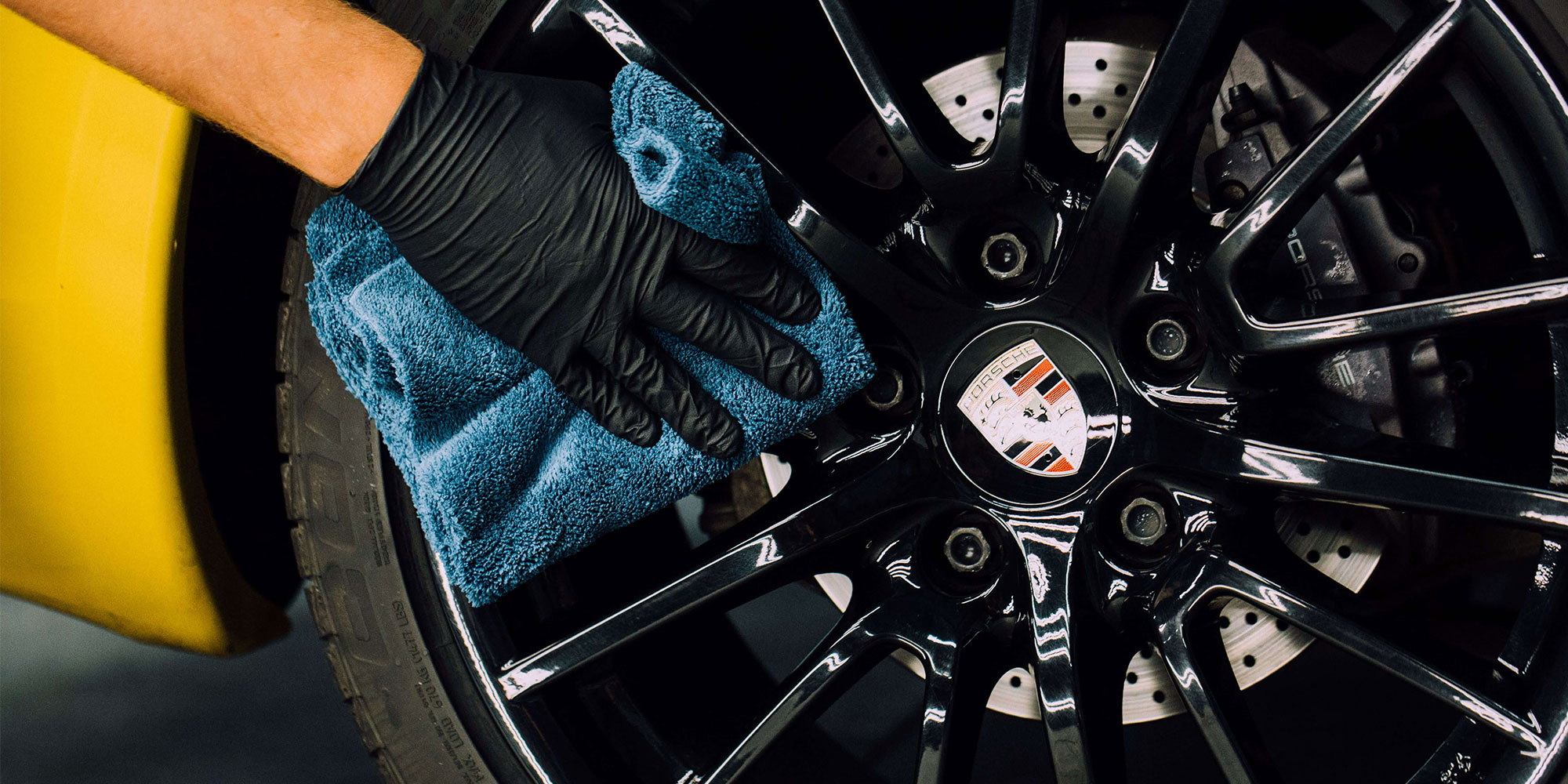 A RestorFX Technician protecting the black rim on the wheel of a yellow sports car with ClearFX Wheels product