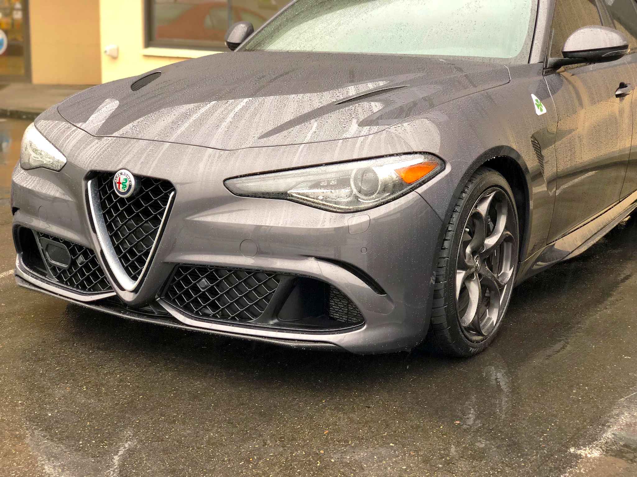 Front of a shiny, reflective and brilliant silver car with beading rain drops on the hood, headlight and side