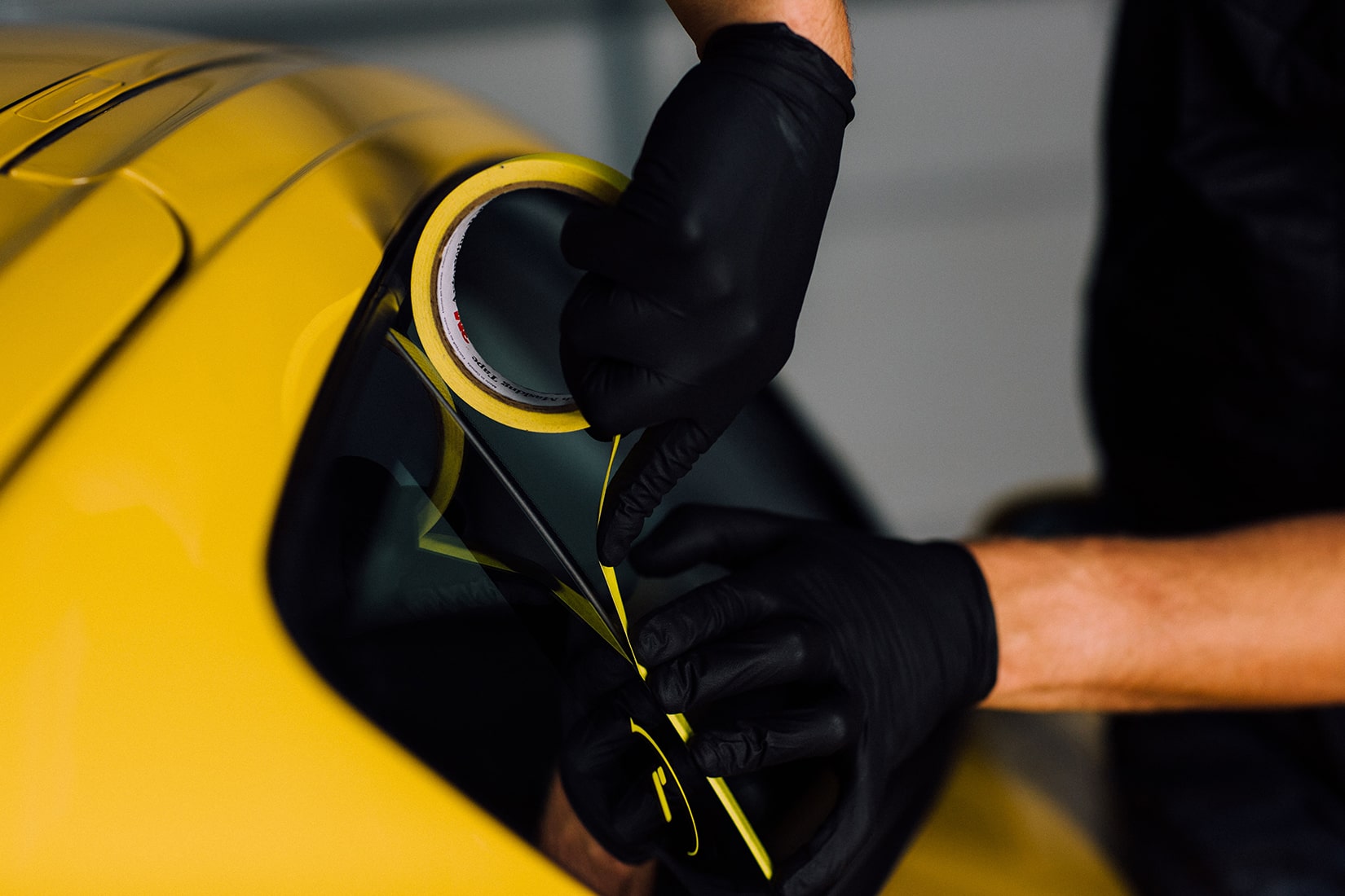 A RestorFX technician taping off the window trim of a yellow sports car to prepare the vehicle for paint restoration